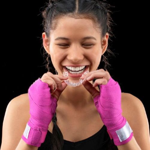 Woman wearing pink boxing gloves putting invisible teeth aligners in. 