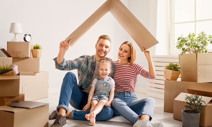 A family smiling under a piece of folded cardboard pretending like it is a roof