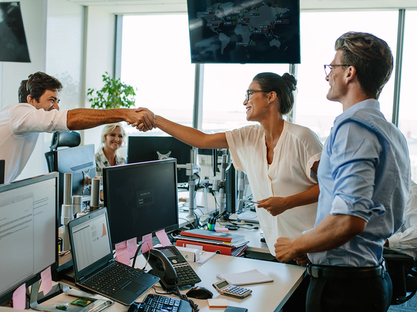 tech team shaking hands over computer monitors