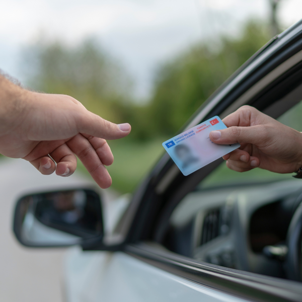 person handing their driver's license to someone out a car window.