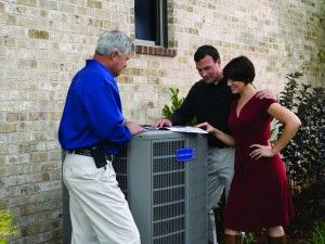 Image of a man and woman standing with a technician over a large ac unit