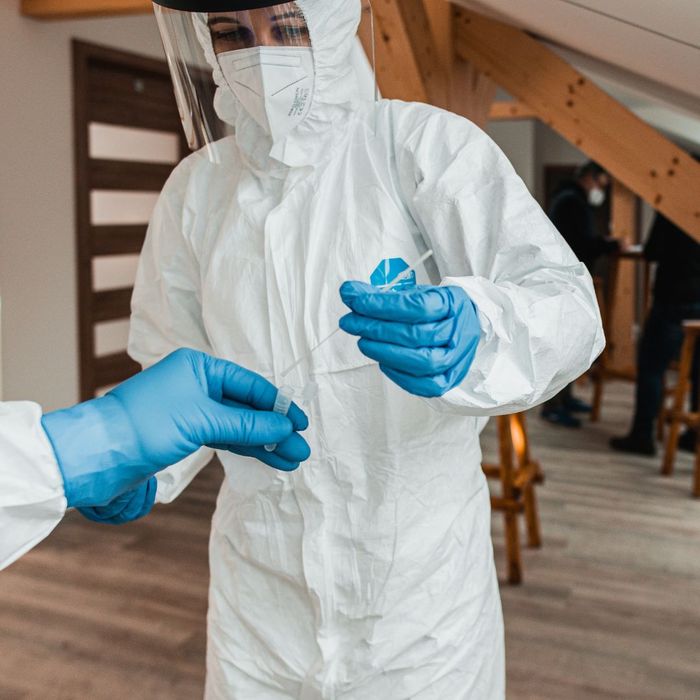 a person in a full hazmat suit, mask, and gloves putting a sample into a test tube to test for asbestos