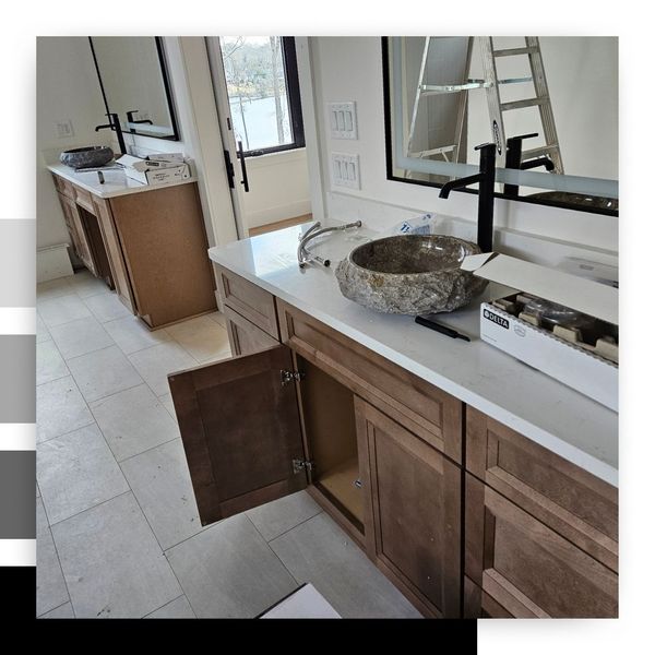 Double vanity cabinet in progress during a bathroom renovation, featuring brown wood cabinetry, white quartz countertops, black modern faucets, and unique, rustic stone vessel sinks.