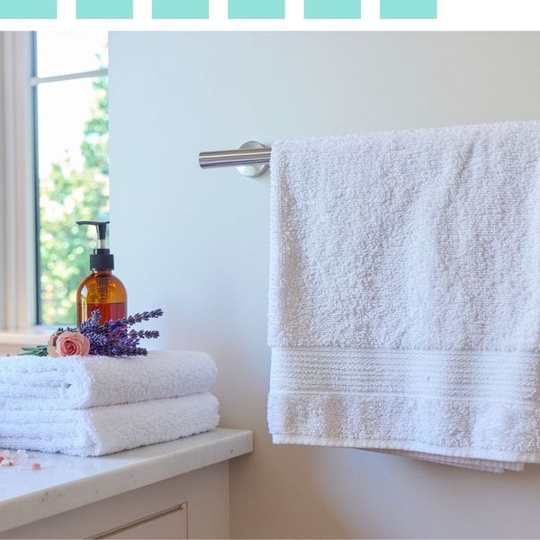 Freshly laundered white towels stacked on a marble bathroom counter next to a lavender sprig and soap dispenser.