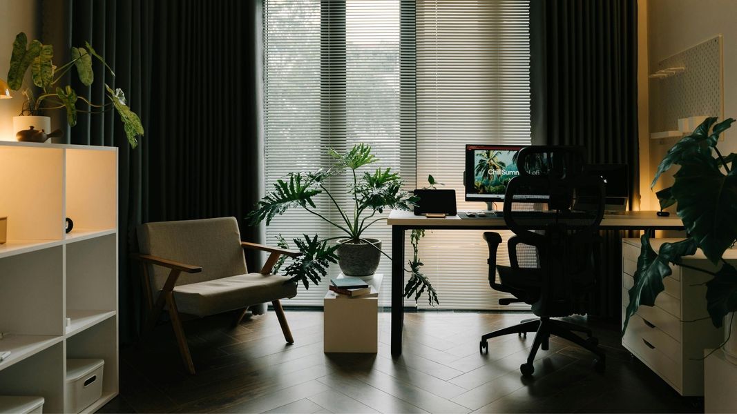 Modern home office with dark curtains, indoor plants, and a clean white desk, showcasing a tidy workspace after a maintenance cleaning.