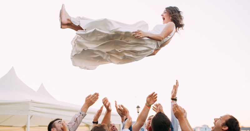 A wife being tossed into the air by men at her reception
