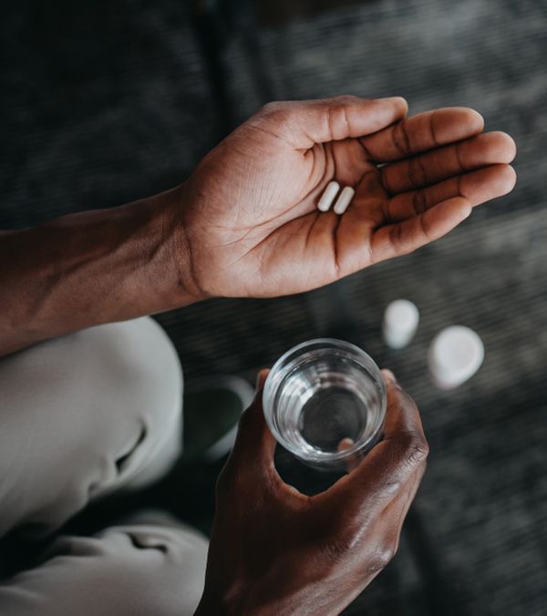 A man holding two supplement pills and a glass of water