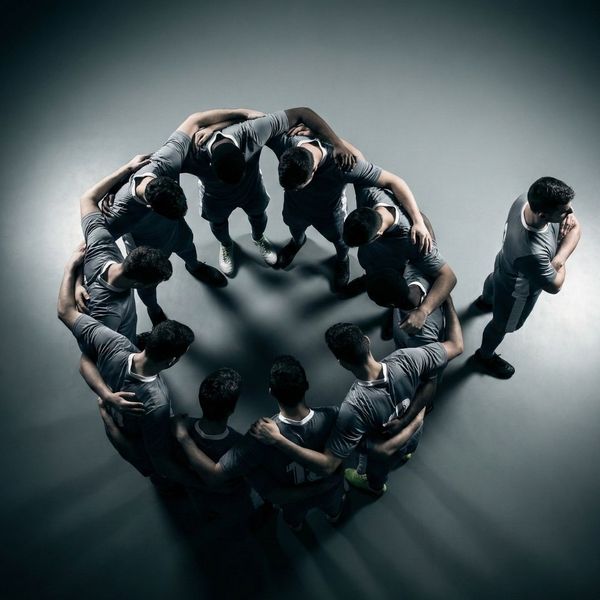 Overhead view of sports team huddle showing subtle signs of hidden conflict and isolation.