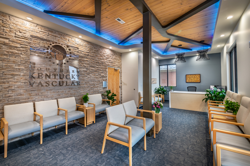 The welcoming, modern waiting room and reception desk at Southern Kentucky Vascular, featuring a textured stone wall with the clinic's logo.