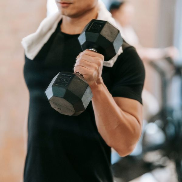A person in a black t-shirt with a white towel over their shoulder lifts a black dumbbell in an apartment complex gym Best Amenities for Remote Workers Best Amenities for Remote Workers 2.jpg