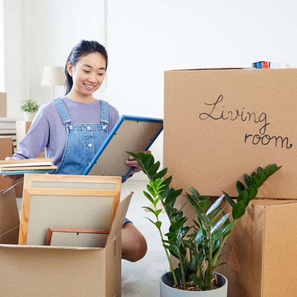 Woman unpacking a box that says "Living Room," smiling. 