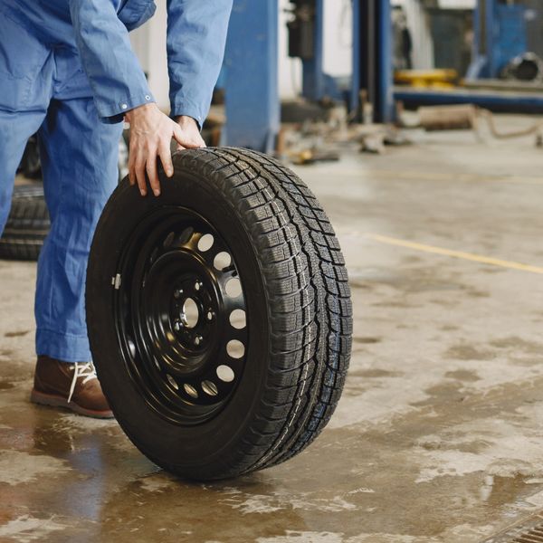 A mechanic rolls a winter tire mounted on a black steel rim across the floor of a garage.