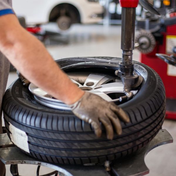 A mechanic uses a professional tire mounting machine to install a tire onto a silver alloy rim in an auto service center.