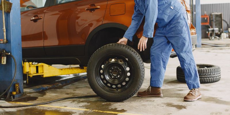 man removing tire from car in auto shop