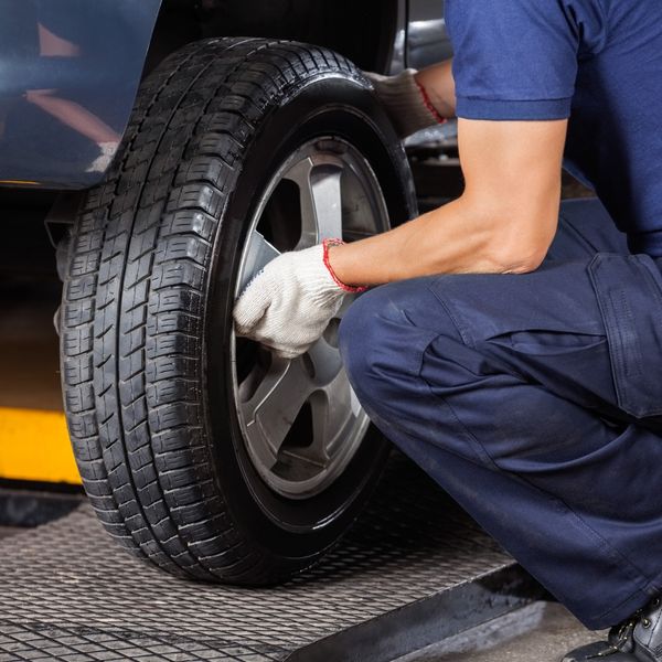 A close-up of a technician in work gloves tightening the lug nuts on a car's alloy wheel with a lug wrench.