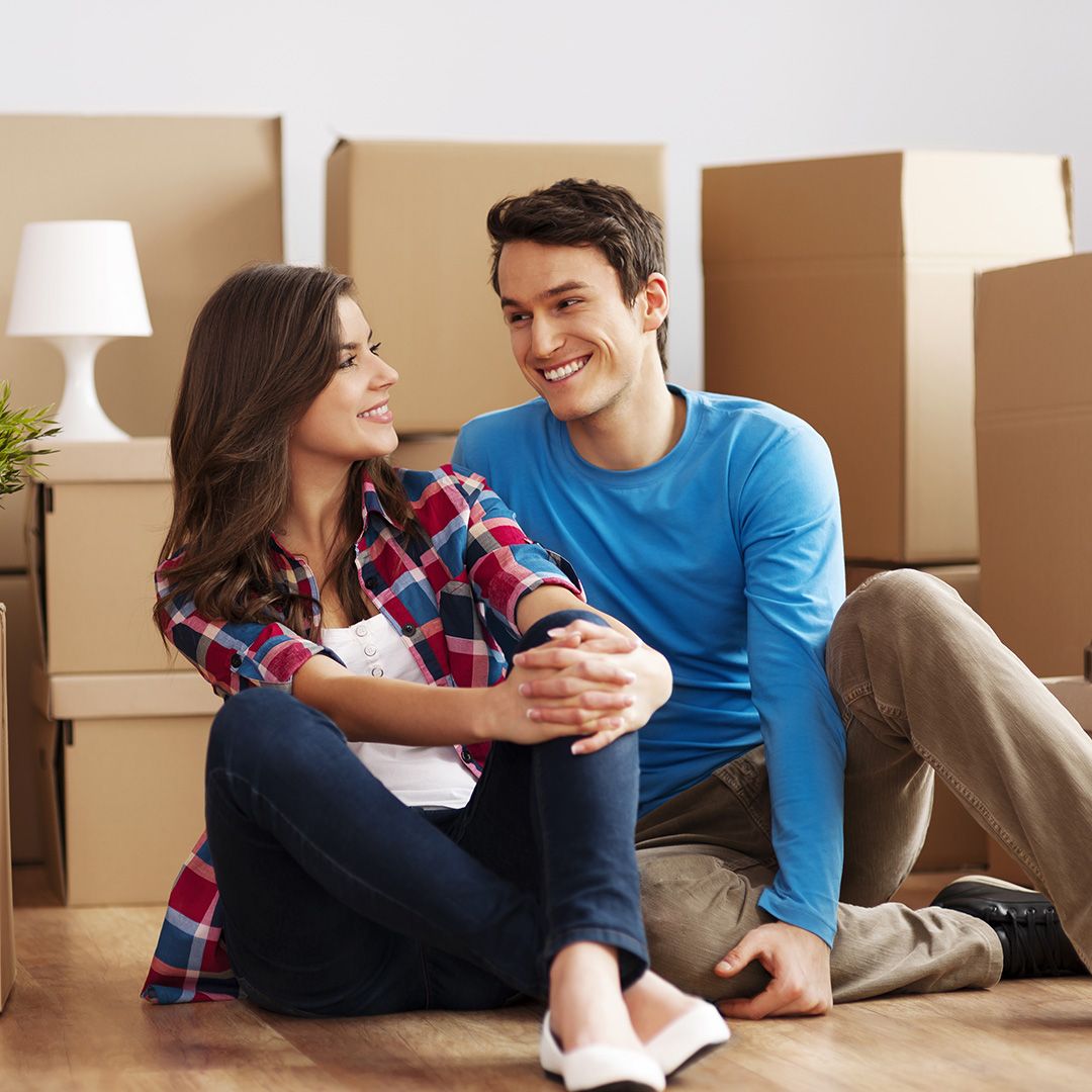A couple sitting on the floor with moving boxes behind them