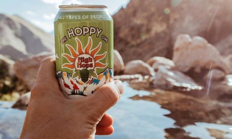 The Hoppy One Can being held up in front of mountains