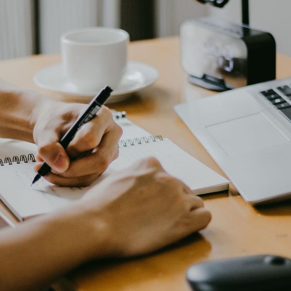 Writing in notebook beside laptop and coffee cup