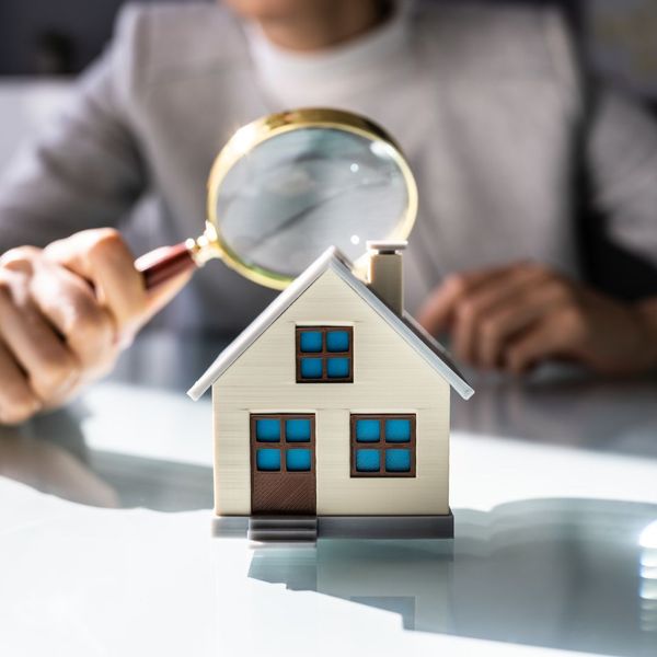 Person looking at a small model home with a magnifying glass