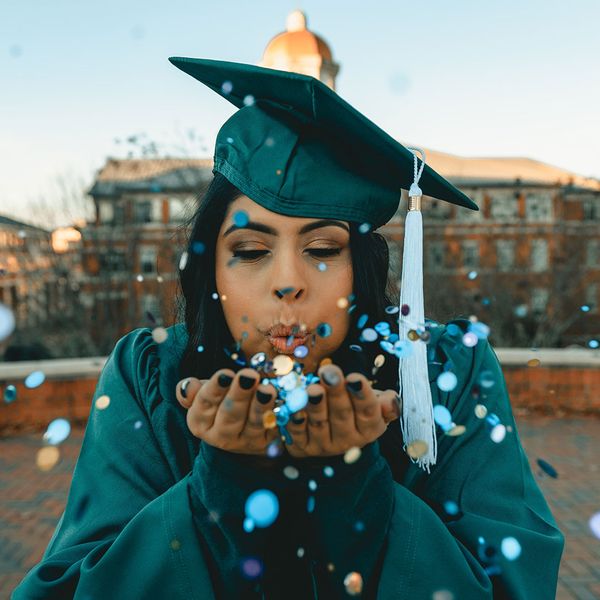 a woman in a graduation gown blowing confetti