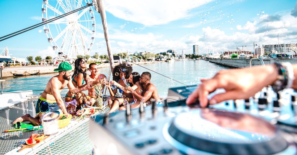 a group of people cheering on a boat deck with a dj playing in the background