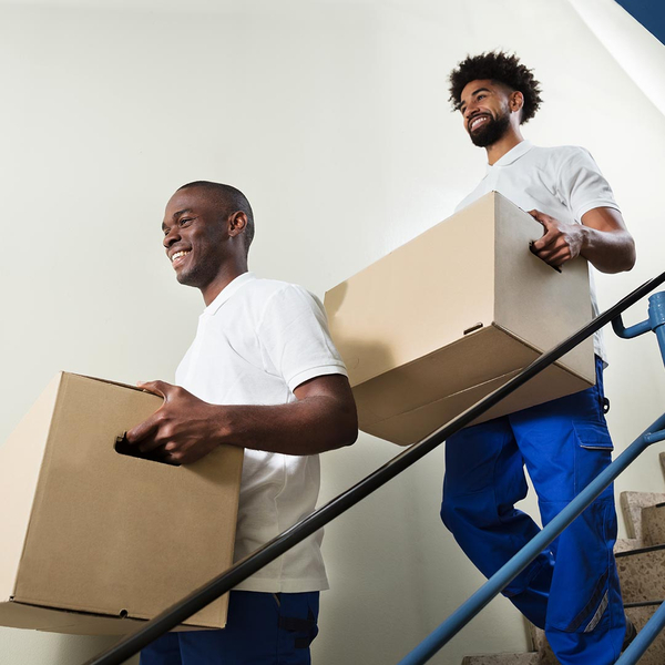 two smiling movers carrying boxes down stairs