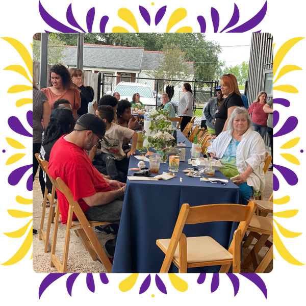 A diverse group of people sitting around a long, navy-blue covered table in the covered outdoor patio