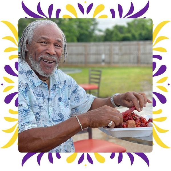 Smiling man in a Hawaiian shirt enjoying a plate of boiled crawfish in the grassy outdoor gathering area,