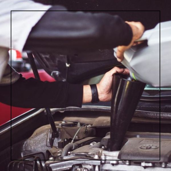A person wearing a long-sleeved shirt is pouring oil from a silver bottle into a car's engine using a black funnel. A person wearing a long-sleeved shirt is pouring oil from a silver bottle into a car's engine using a black funnel.