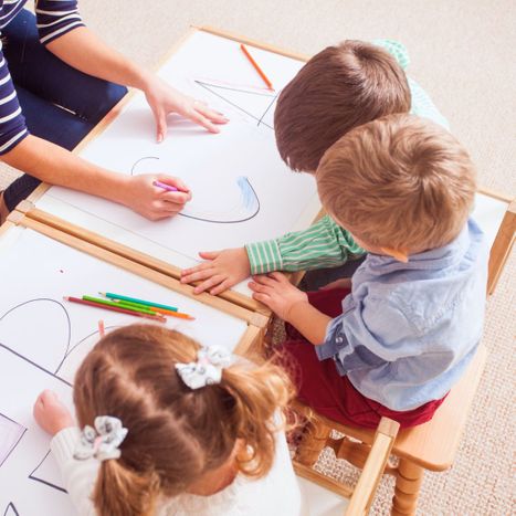 a group of toddlers coloring large sheets with letters on them