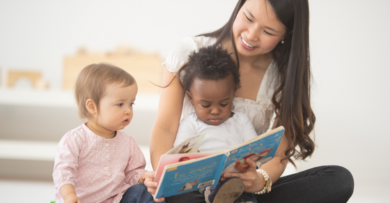 Daycare teacher reading to two infants. 