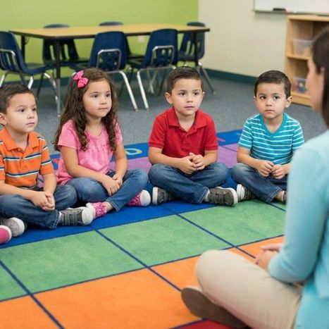 A group of five pre-k children sitting calmly in a circle listening to a teacher.