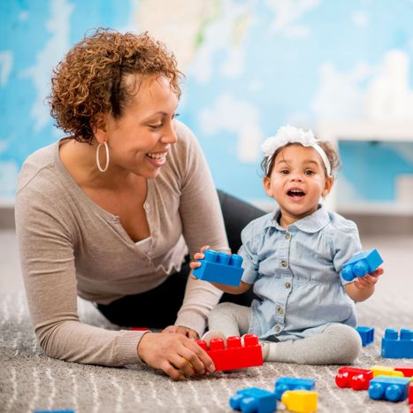 Preschool teacher sitting on the ground with an infant. 