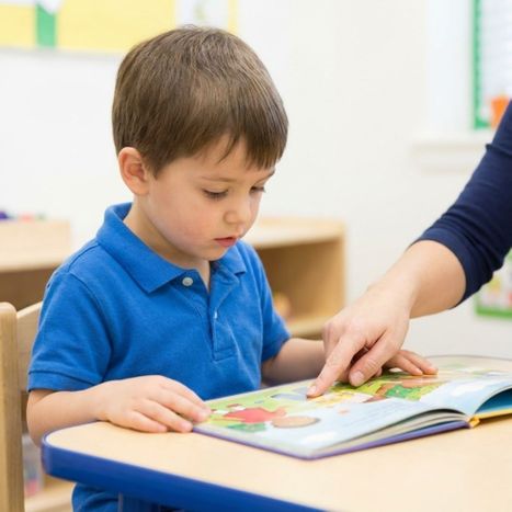 A young boy reading a picture book with a teacher's guidance.