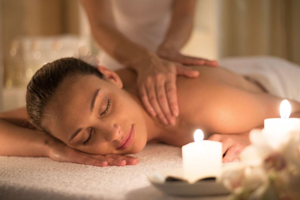 a woman relaxing on a massage table with candles as she gets a massage