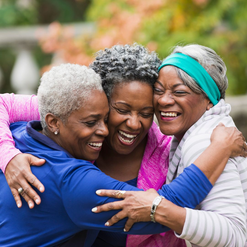 Three senior women hug and laugh
