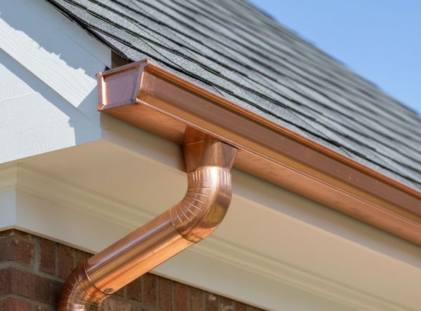 Close-up of a newly installed copper gutter section gleaming in the sunlight, perfectly mounted against the roofline of a residential house.