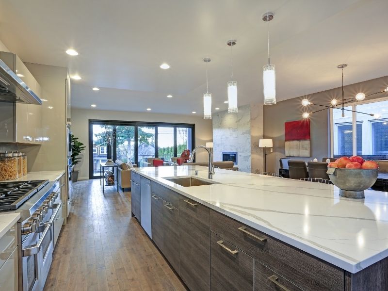A large modern kitchen island with a white marbled waterfall countertop and dark wood cabinetry.