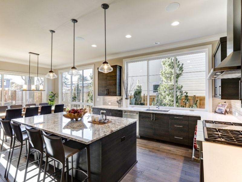 A dark wood kitchen island with a speckled granite countertop and four black leather barstools.