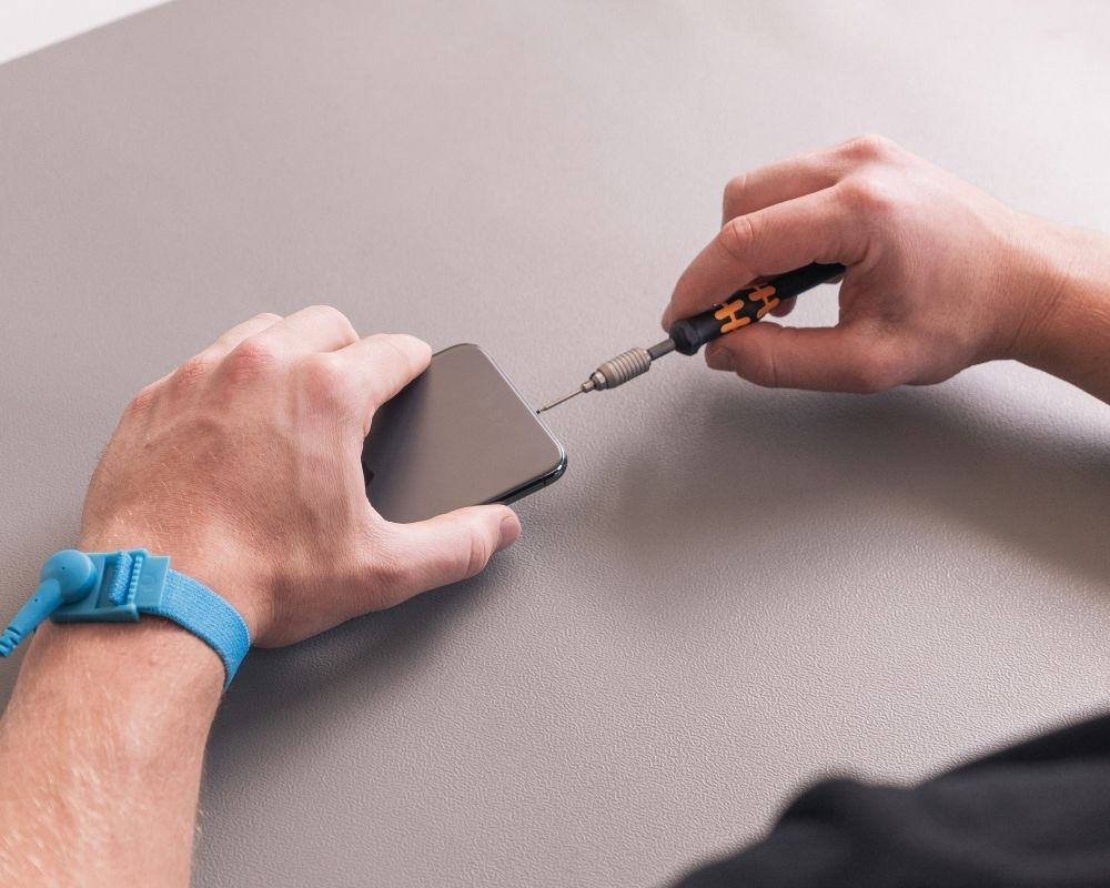 Precision mobile device repair showing hands using a micro-screwdriver on a smartphone.