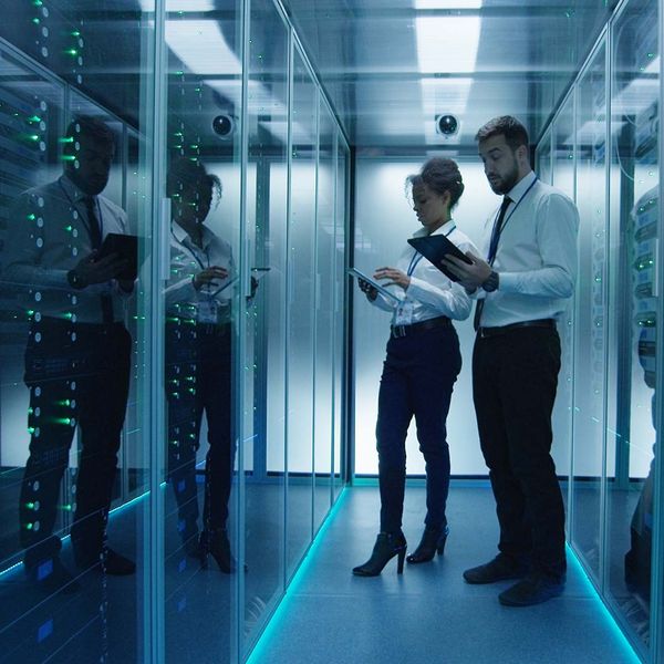 Side view of multiethnic men and women with tablets coworking in data center server room checking hardware.