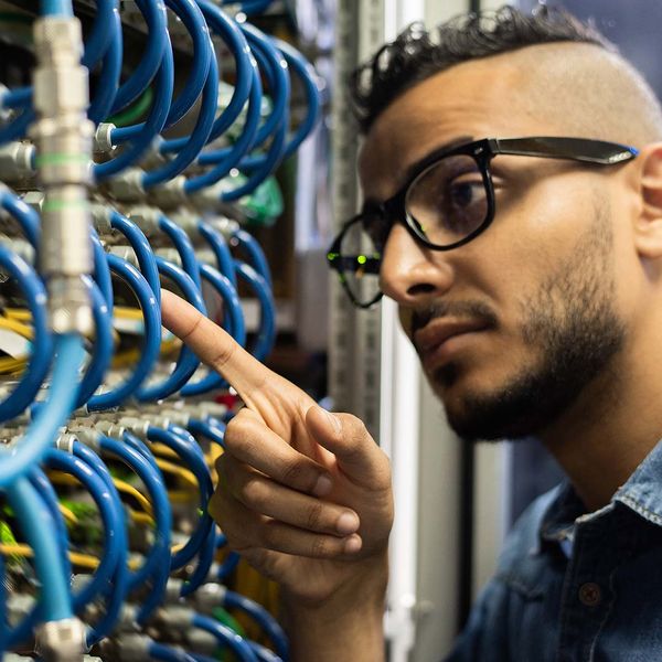 Network engineer with beard pointing at cable and checking IT in server room.