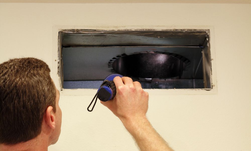 person examining duct with flashlight