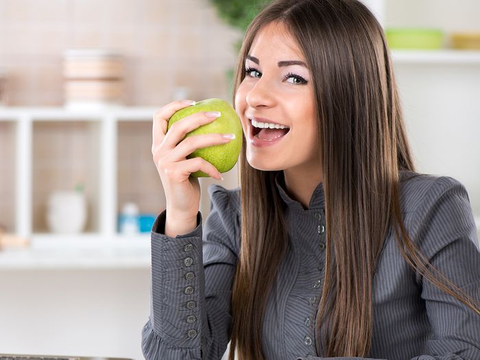 An image of a young woman eating a green apple at her work desk