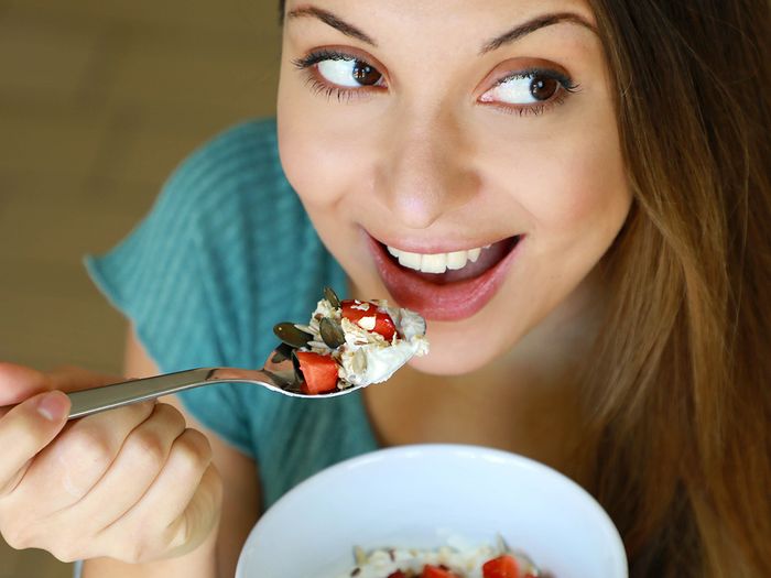 An image of a young woman eating a bowl of yogurt and fruit