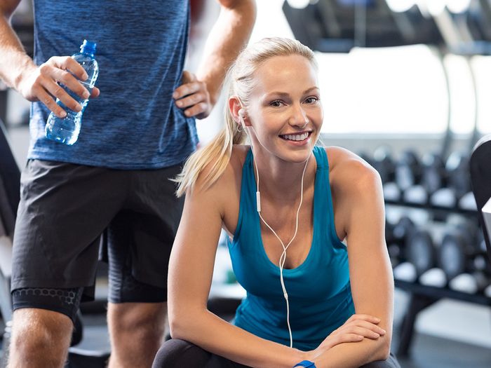 An image of a healthy young woman smiling while relaxing on a bench at a fitness center.