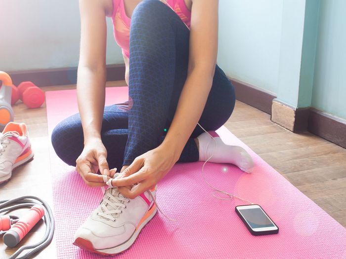 Image of a woman sitting on a workout mat putting on her shoes