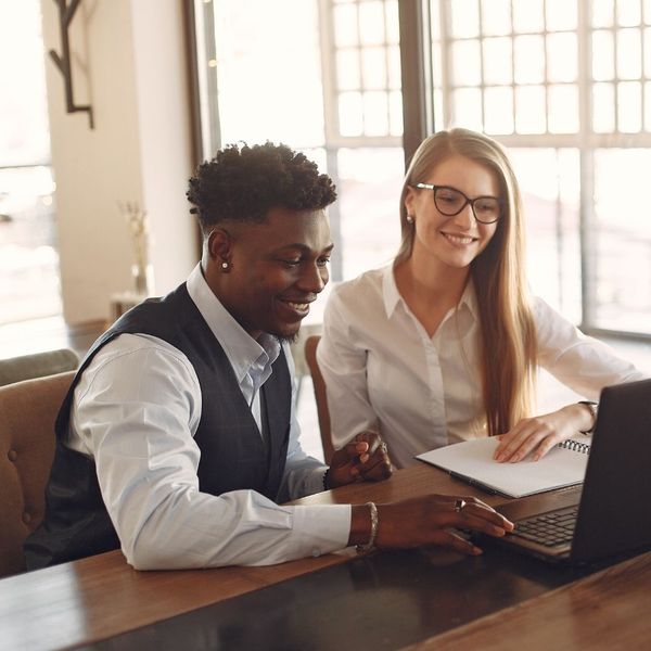 A supportive male manager leaning over to discuss work and ask questions with a female employee at her desk.