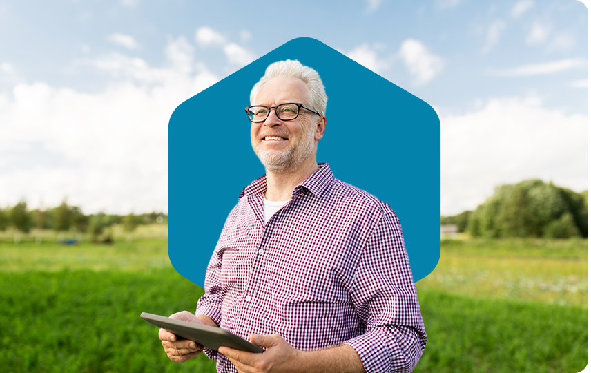 A farmer in a green field smiling while holding his tablet