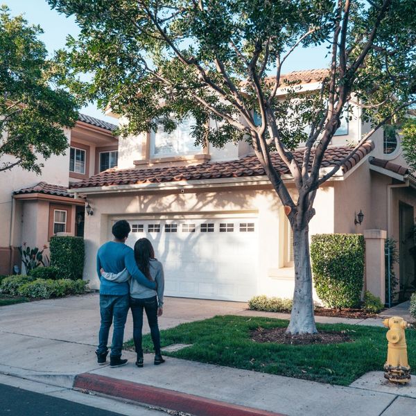 A couple stands in their driveway and looks proudly at their home